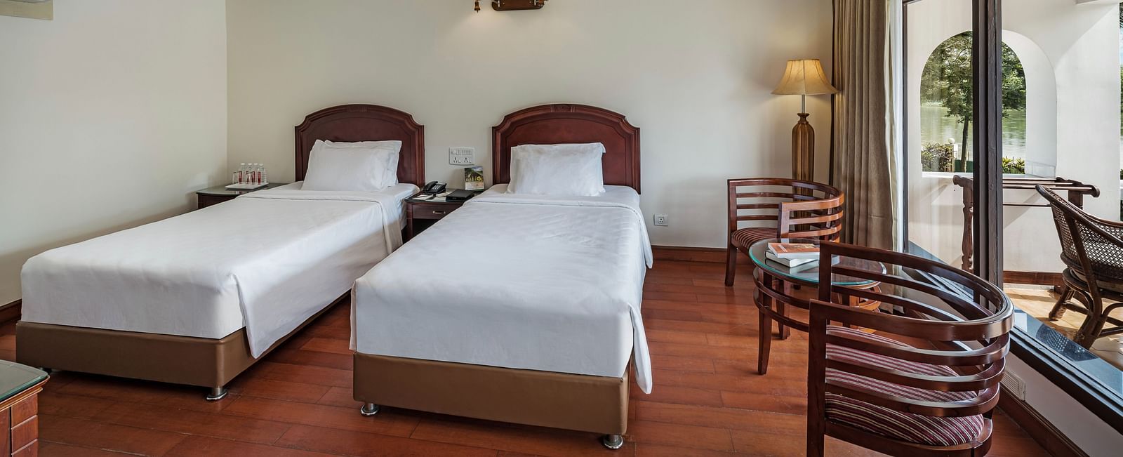 An image of the River View Room With Verandah featuring two single beds, bed side table, lamps, and chairs - GReaT Trails River View Resort Thanjavur By GRT Hotels