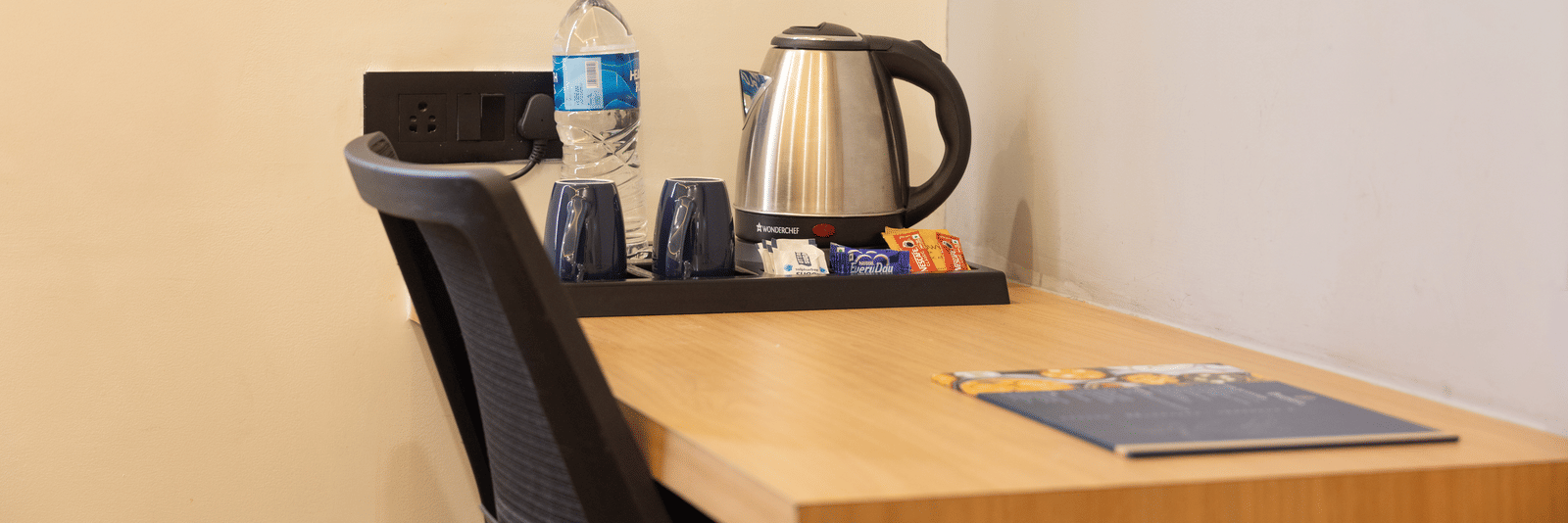 Interior of a guest room showing the desk area with a kettle and refreshment supplies at Pravasa Stay Luv Kush, Indore.