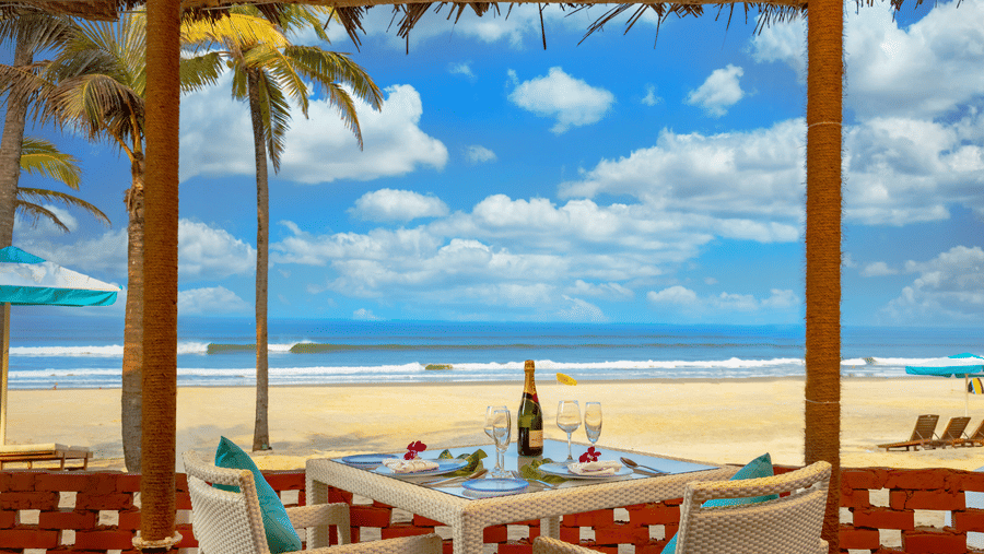 chairs and a table inside a shack with blue sky and sea in the background - Caravela Beach Resort Goa