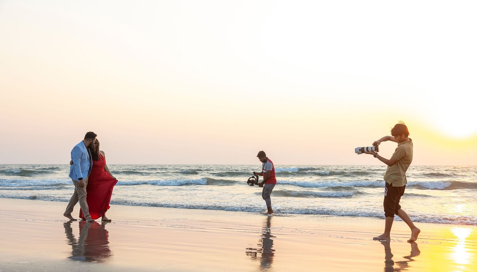 a couple being photographed on the beach with the evening sun in the background - Caravela Beach Resort Goa