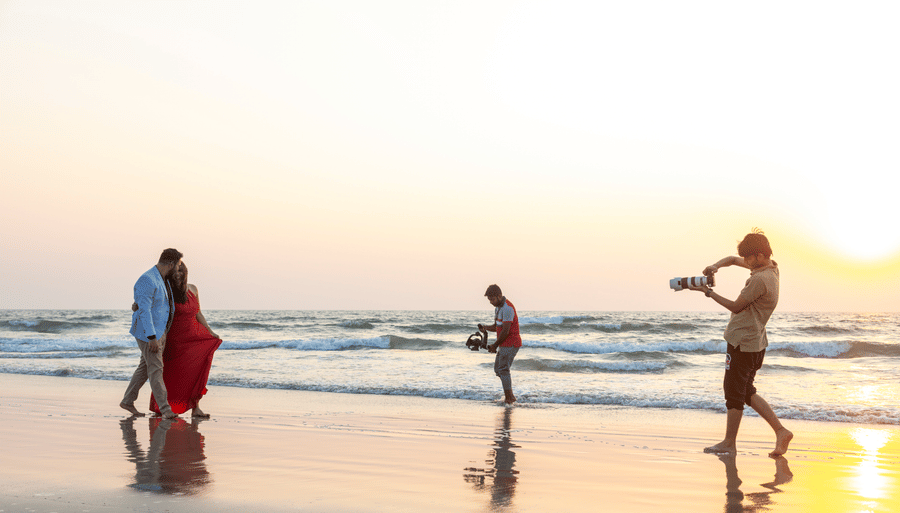 a couple being photographed on the beach with the evening sun in the background - Caravela Beach Resort Goa