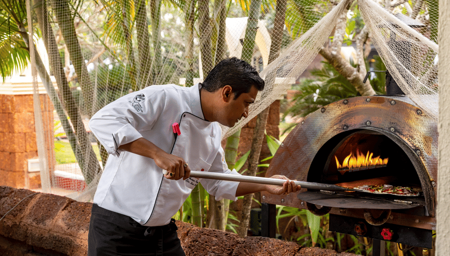 a chef sliding a pizza to cook in a wood-fire oven - Caravela Beach Resort Goa