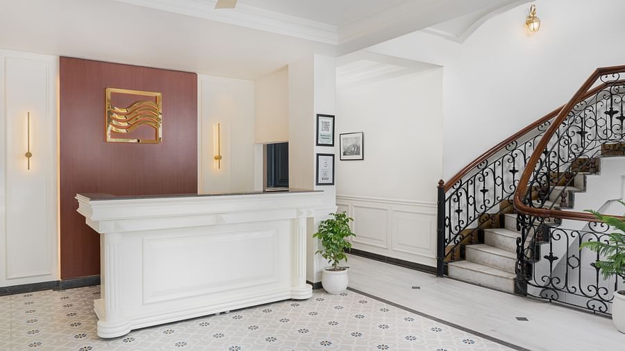 Reception area with a large desk with a potted plant to the side and a staircase on the right | Hotel Ganga Maiya
