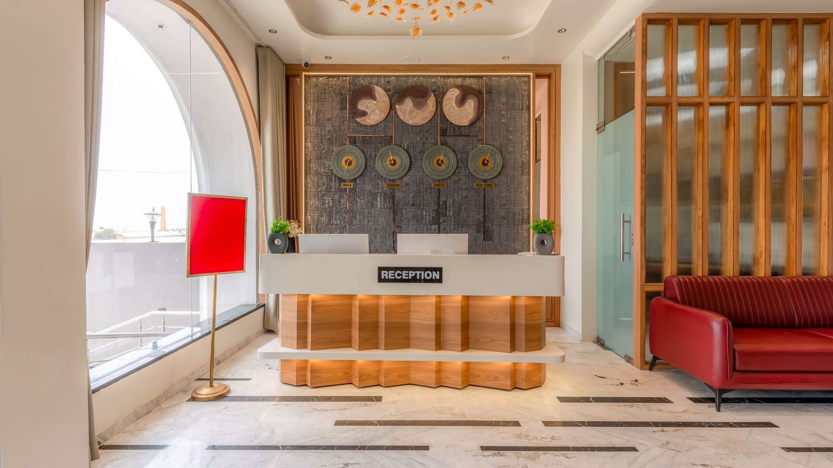 Reception desk at Pride Elite Dwarka which also features clocks of different time zones, a sofa on one side and on the other there is a lamp.