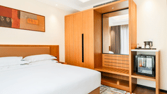 Standard Double Bed Room at Bamus Sarovar Portico, Kampala, with a double bed, wooden wardrobe, wall art, and a small refrigerator under a counter.
