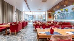 A restaurant featuring well furnished seating area with tables, chairs, and sofa chairs, AC, lights, and  glass walls at Pride Elite Dwarka.