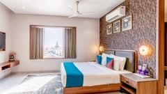 Suite Room at  Pride Elite Dwarka featuring a bed, a bedside table with lamp, photo frames on the wall, an AC, a flat TV screen, and an open window.