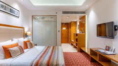 Superior room featuring a plush bed in front of a Tv mounted on the wall and a bathroom with frozen glass