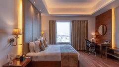 Wooden floor suite featuring a plush bed in ambient lighting with lamps on both sides of the bed and daylight making its way through the large window