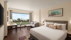 A bedroom at Sarovar Portico, Hanumangarh, with a bed, a window with a view, and a table.