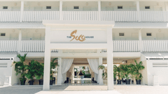 The entrance to The Soco House featuring white architecture, draped curtains, and tropical plants and The Soco House logo.