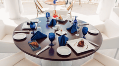 A neatly arranged round dining table with crockery and white chairs in a natural light setting at The Soco House restaurant.