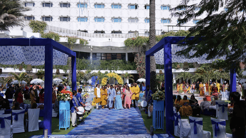 Guests walking through a beautifully decorated outdoor wedding venue featuring floral arrangements, ceremonial drummers, elegant seating, and vibrant event decor at Clarks Amer, Jaipur.