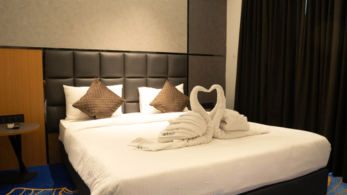 Comfortable bedroom at Magnus Lxia Premier, Kalyani Nagar with plush bedding, elegant décor, and towel art on the bed.