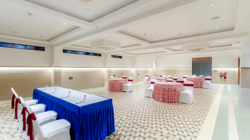 Banquet Hall at Pride Elite Dwarka featuring conference table with chairs, and other sets of tables and chairs decorated with ribbons and fabrics for guests.