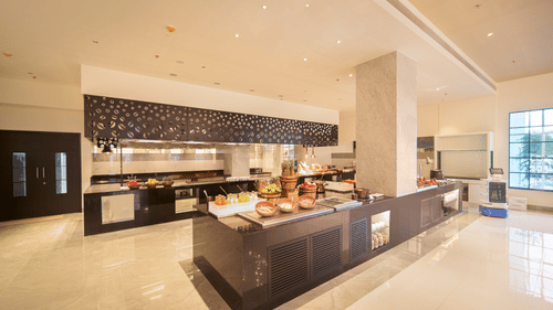 A contemporary dining area features a long counter with bar stools and various food preparation stations | SPR Kitchen | Sarovar Portico, Sriperumbudur