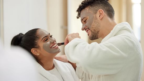 A happy couple wearing white bathrobes, undergoing spa treatment while having a face mask.