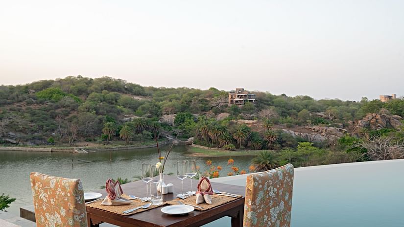 A table for two set next to the swimming pool with views of the forest next to the lake - Chunda Shikar Oudi, Udaipur