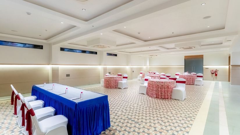 Banquet Hall at Pride Comfort Dwarka featuring conference table with chairs, and other sets of tables and chairs decorated with ribbons and fabrics for guests.