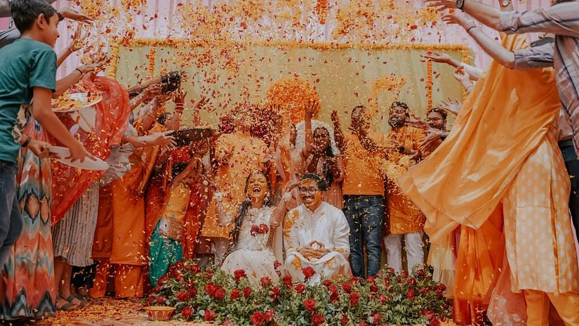 A bridge and groom inside a kalyana mandapam where people are celebrating by throwing flowers