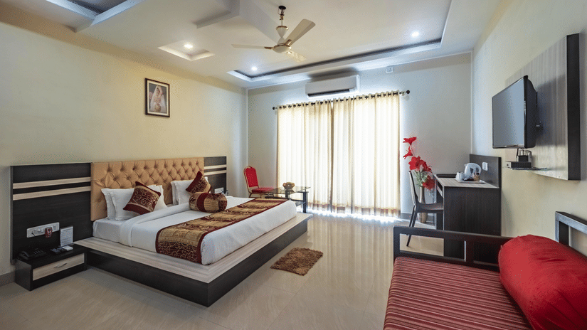 Modern room with tufted headboard, king bed, red cushioned bench, desk with flowers, TV, and balcony doors at Viceroy Beach & Spa Resort, Mandarmani.