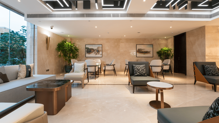 Lobby of Bamus Sarovar Portico, Kampala featuring big glass windows offering views of the surroundings. The lobby is seen well-lit with ample seating and cushioned chairs.