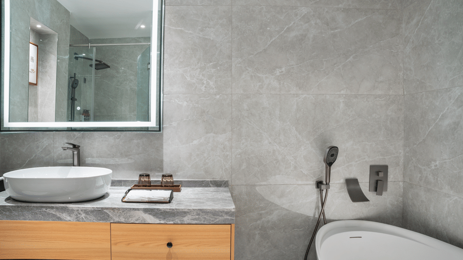 A tiled bathroom featuring a sink on a wood vanity and a soaking tub at Bamus Sarovar Portico, Kampala.