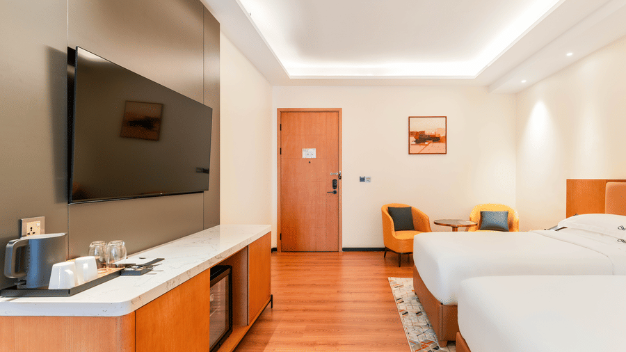 A wall-mounted television across from twin beds and a doorway at Bamus Sarovar Portico, Kampala.