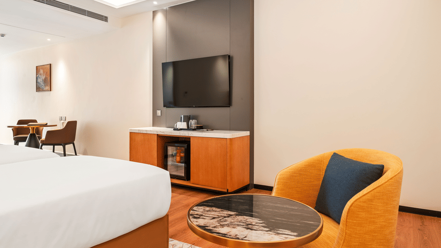 An armchair next to a round coffee table and a television console in a room at Bamus Sarovar Portico, Kampala.