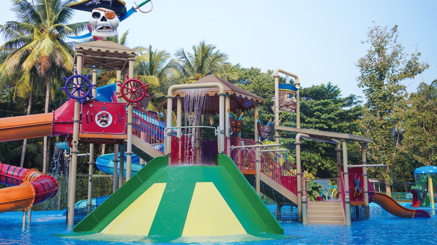 A colourful pirate-themed water playground with slides, splash features, and a skull-shaped structure at a water park, surrounded by palm trees.