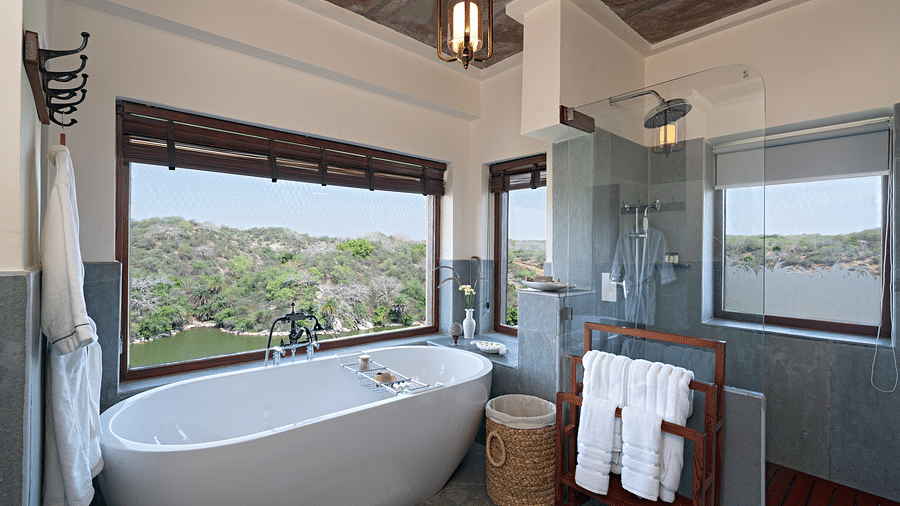 a bathtub with a floor to ceiling window showing the forest cover inside one of the rooms - Chunda Shikar Oudi
