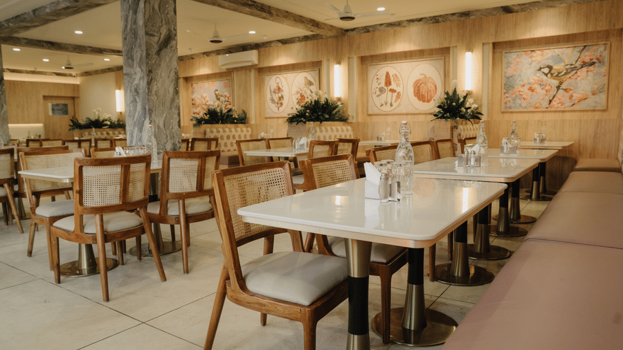 Restaurant with neatly arranged dining tables, wooden chairs, cushioned seating, and warm ambient lighting at Corbett Adventure Resort, Ramnagar.