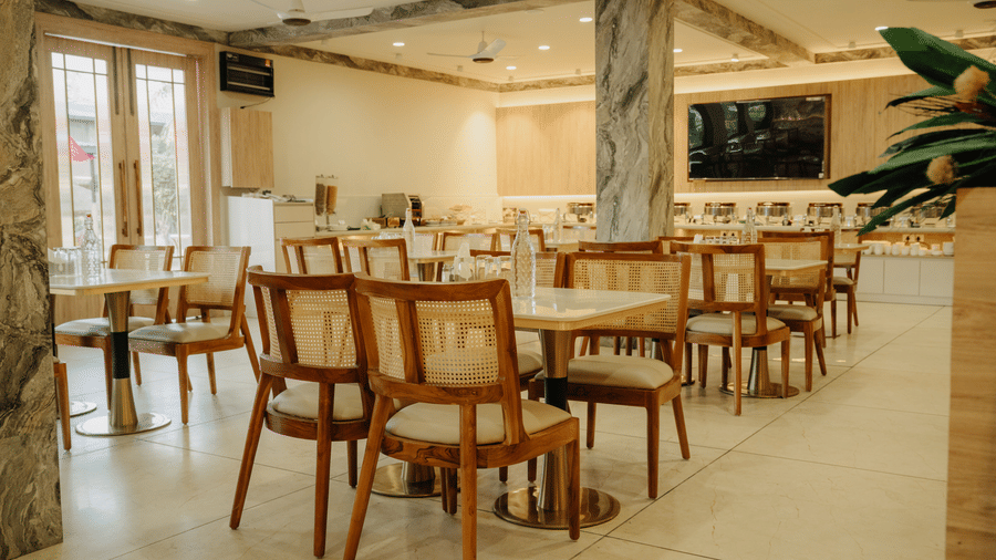Restaurant interior at Corbett Adventure Resort, Ramnagar showing organised table settings, natural tones, and a central buffet area.