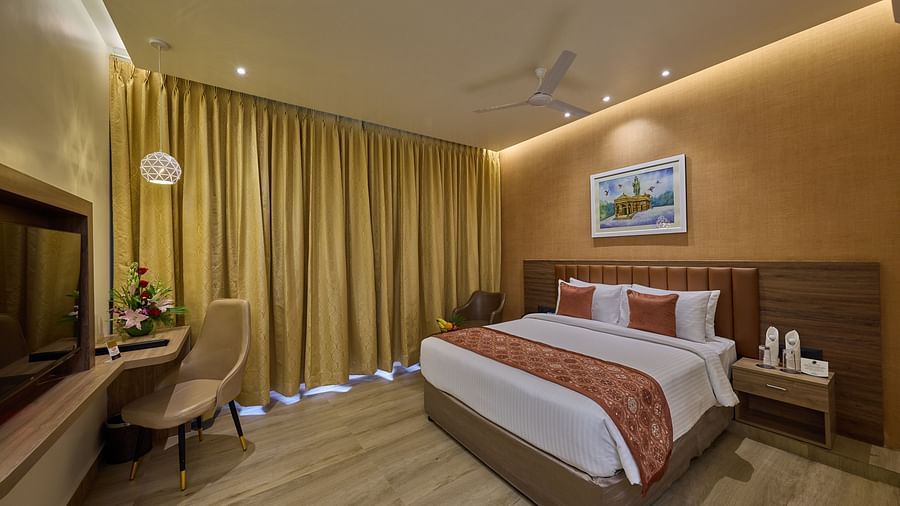 A room with a comfortable bed, a television, black out curtains and a chair