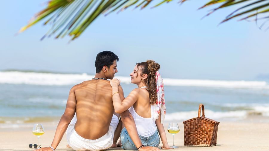 Couple enjoying a romantic beach picnic on the sand with the sea in the background.