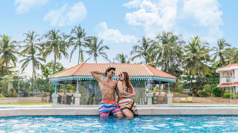 A man and a woman in a tropical outdoor pool surrounded by palm trees.