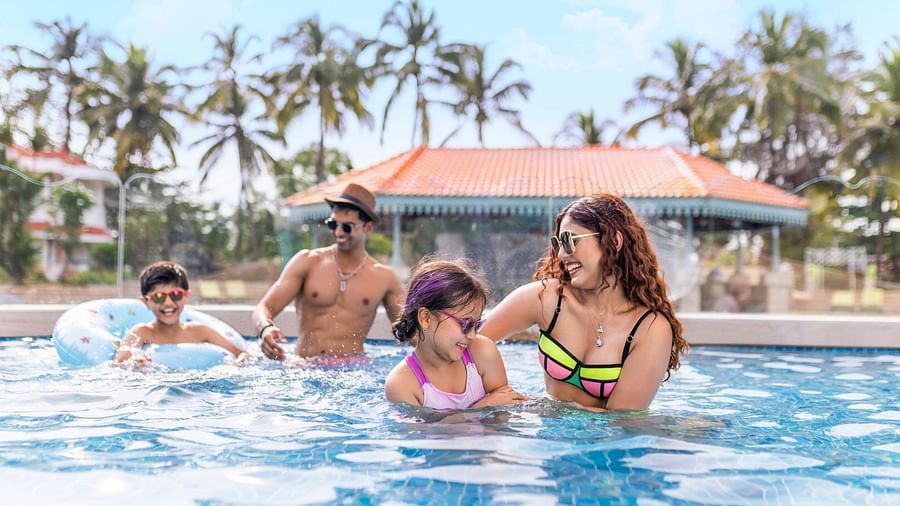 Family enjoying leisure time together in a swimming pool with palm trees in the background.