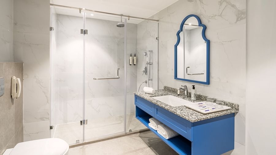 A view of a bathroom with a dedicated shower cubicle, a full-size mirror, a sink, and a phone installed on the wall - MJ Sarovar Portico, Haridwar