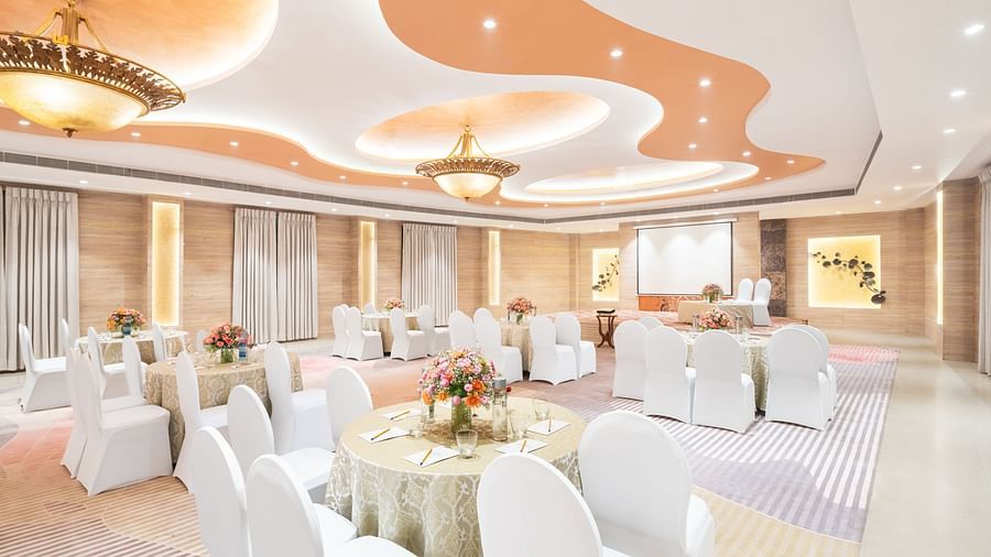 A view of a banquet hall with a high ceiling, soft lighting, and round tables set with white linens and floral arrangements.