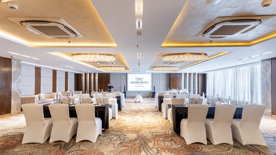 A meeting room at Nirvana Sarovar Portico, Gorakhpur featuring rectangular tables, covered chairs, and chandeliers.