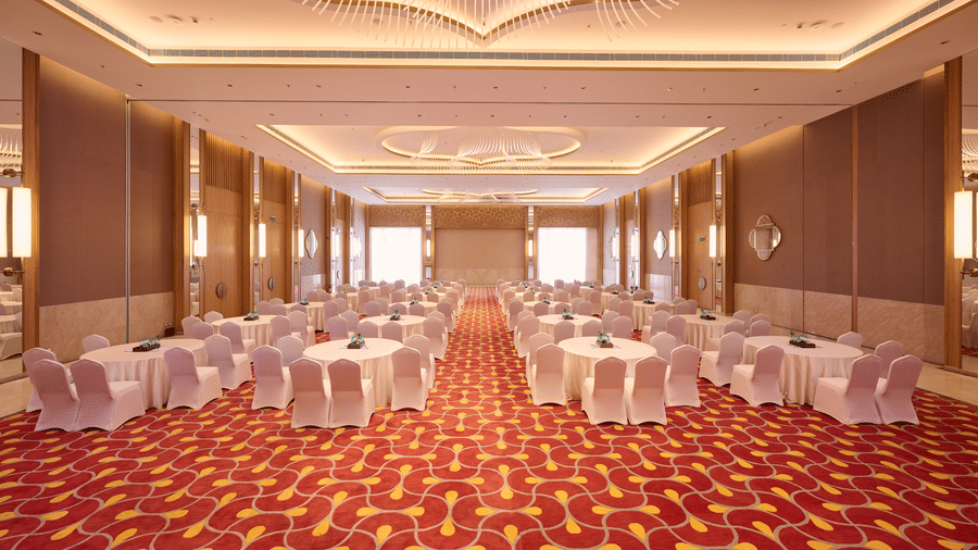 Banquet hall at Prachi Sarovar Premiere, Bhubaneswar, set up with round dining tables, chairs, patterned carpeting, and decorative ceilings.