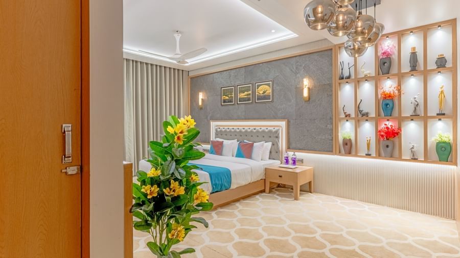Executive Suite at Pride Comfort Dwarka featuring a double size bed, lights hanging from the ceiling, lamps on either side of the bed, and a shelf filled with decorative objects.