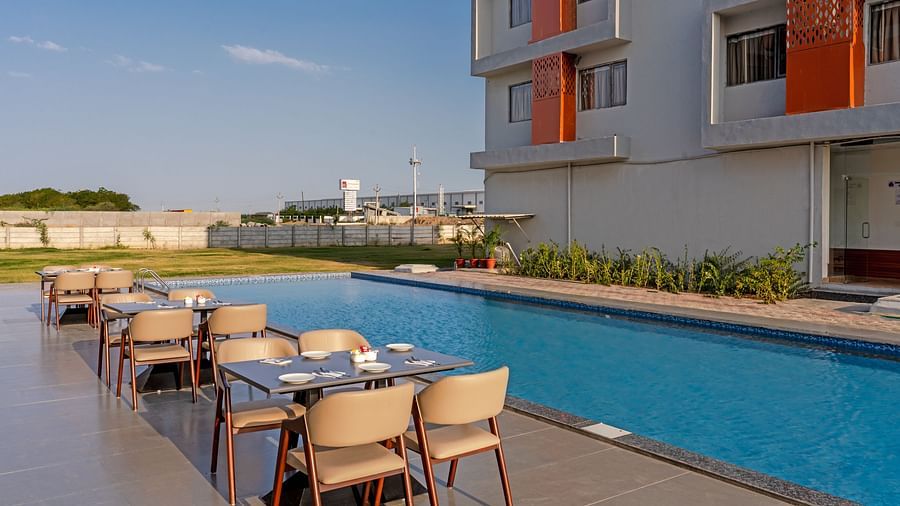 dining tables and chairs across the pool with the hotel in the back of Pride Elite Becharaji