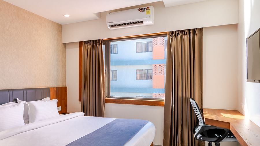 Premium Room at Pride Elite Wellness Resort Becharaji, Gujarat featuring a plush bed next to a window and a work desk in a corner with a chair facing the wall