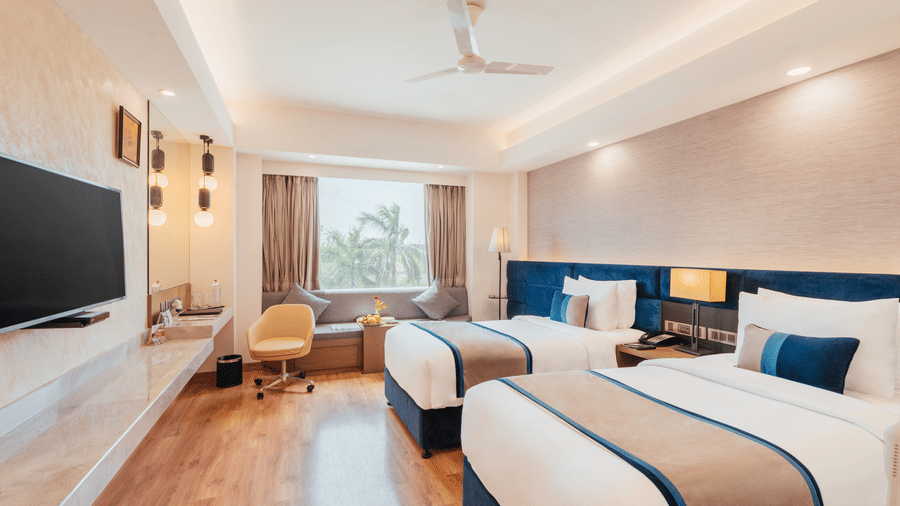 A bedroom with twin beds, padded headboards, workspace unit, and window seating alcove at The Piccadilly Lucknow.