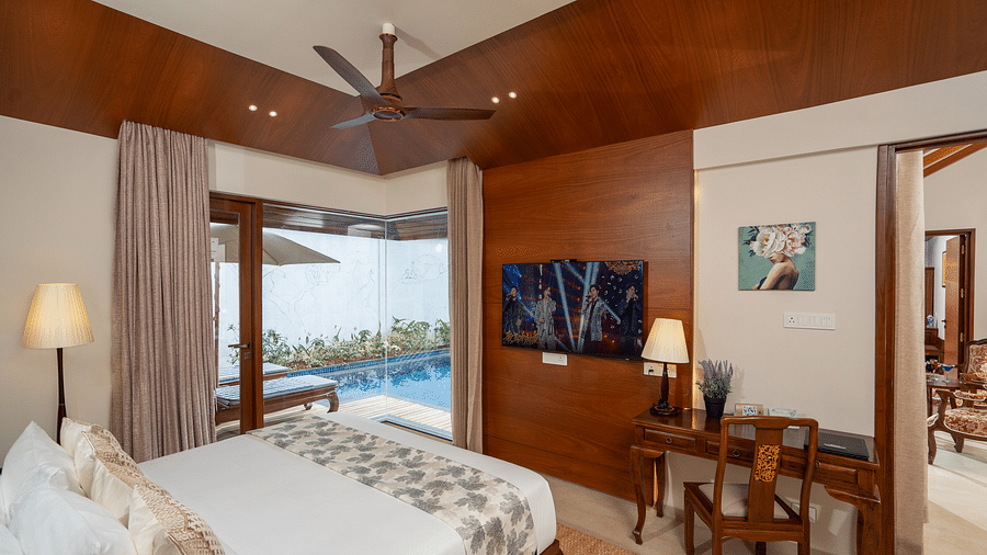 Bedroom of Premium Pool Villa at Uday Backwater Resort featuring a plush bed facing the TV mounted on the wall next to the work desk and the glass window with a pool view