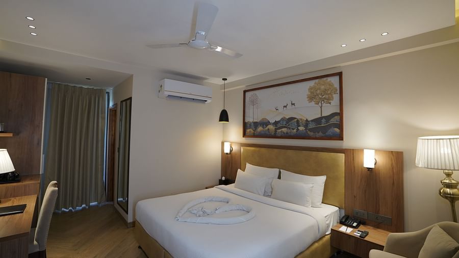 A warm-lit room featuring a king-size bed with a painting above the headboard and an AC mounted next to it
