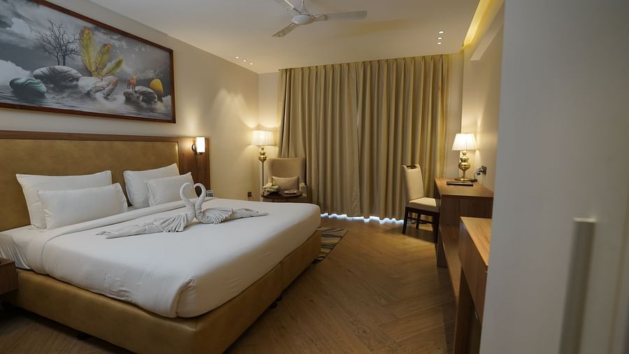 A warm-lit room featuring a king-size bed with a painting above the headboard and a work desk in the corner