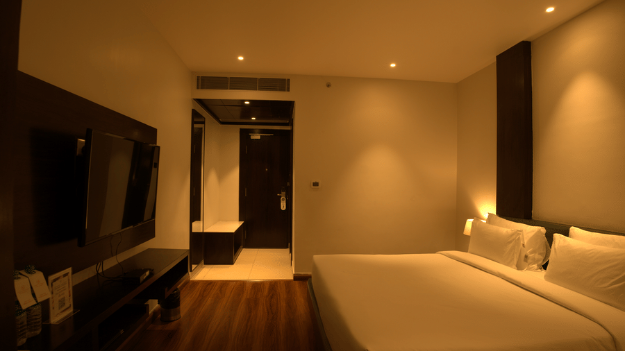 A bedroom at Wedlock Greens Hotels & Resorts, Dhanbad featuring a double size bed, a cabinet table, and a flat TV screen mounted on the wall.