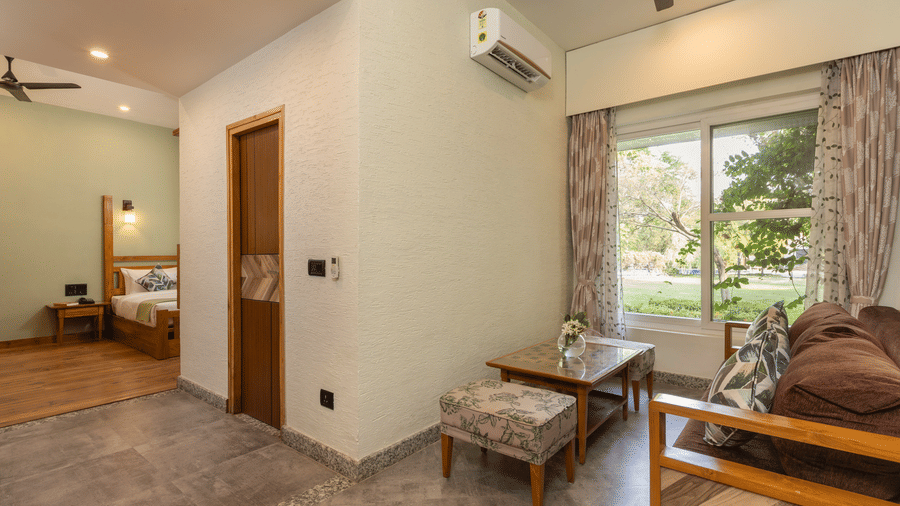 Interior of a Garden Suite featuring a bed, a wooden door, a small seating area with a chair, and a ceiling fan at The Golden Tusk, Jim Corbett